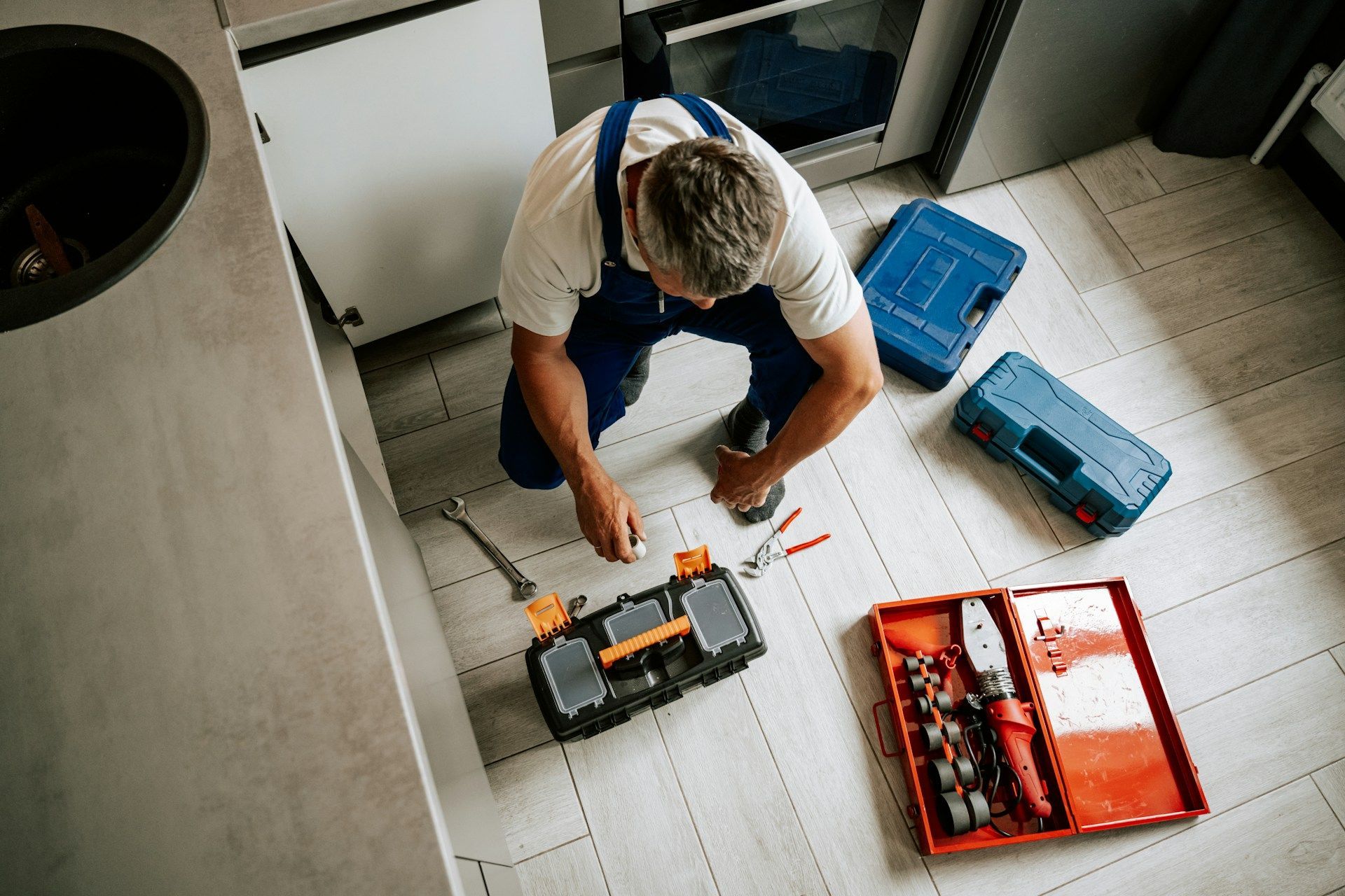 Plumber working under a kitchen sink using a drain cleaning machine.