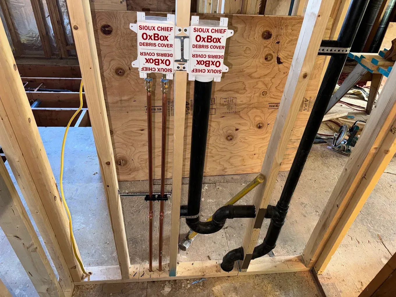 Plumbing pipes and labeled shutoff valves inside an unfinished wall frame under construction