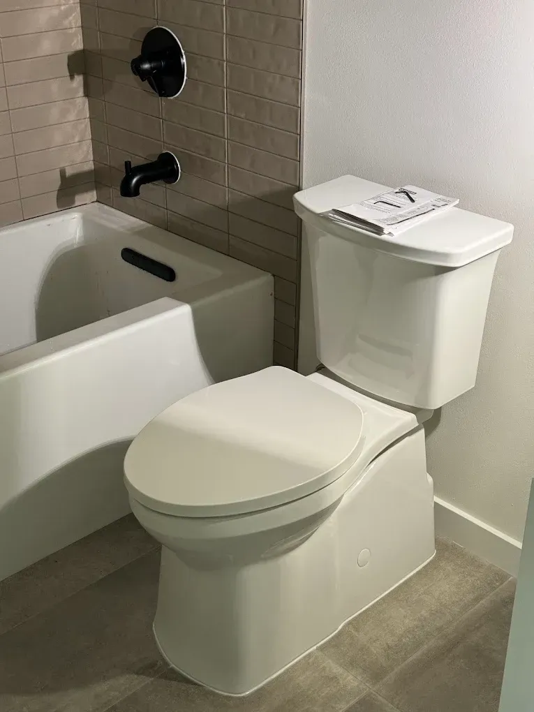 Bathroom with white toilet beside a bathtub, tiled walls, and gray floor.