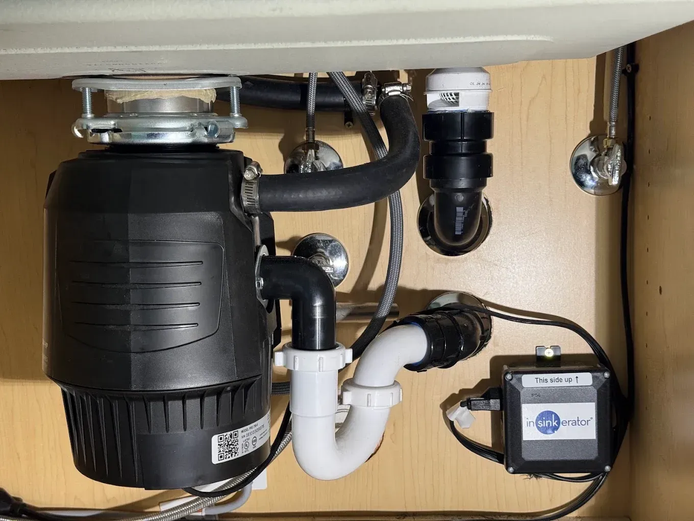 Under-sink plumbing with black garbage disposal, white drain pipes, and a water filter unit.