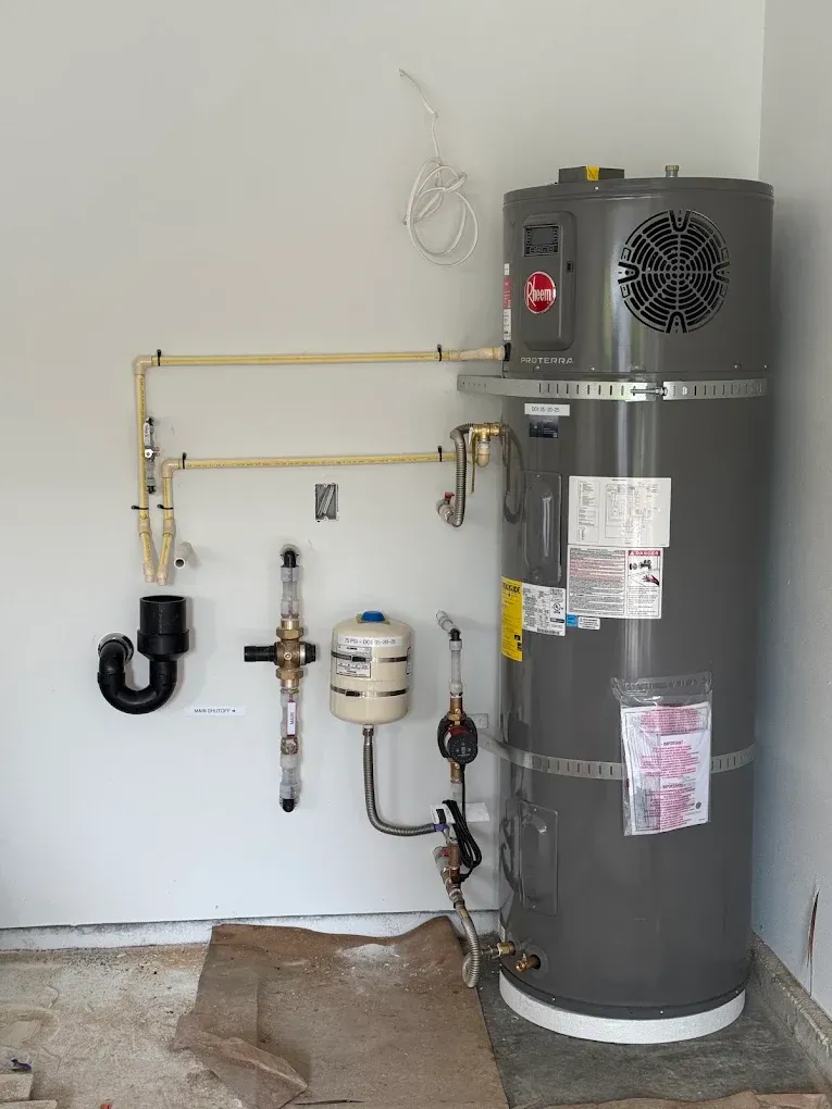 Water heater and plumbing setup in a utility room with exposed pipes and a gas line on a wall.