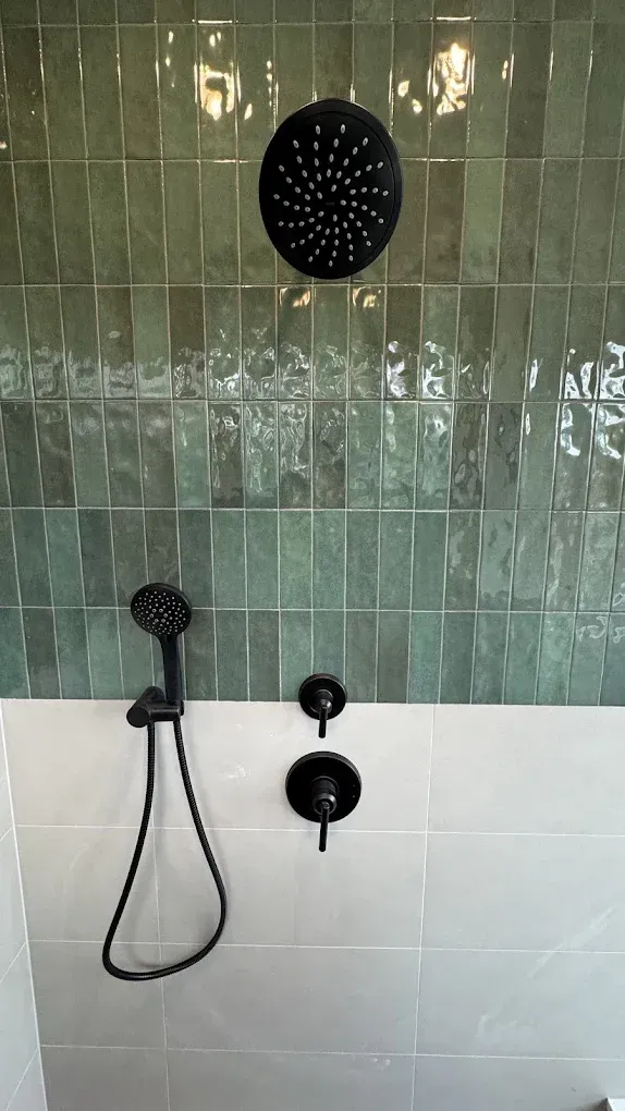 Bathroom shower with green tile wall, black rain showerhead, handheld sprayer, and white lower tiles