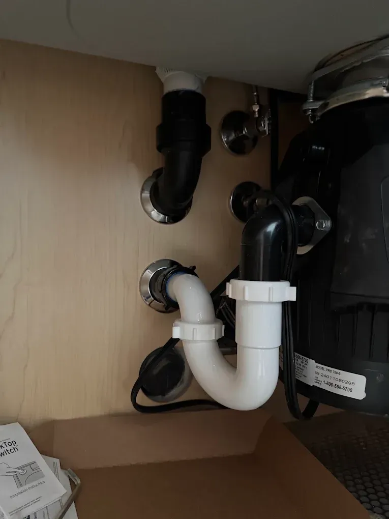 Under-sink plumbing with black and white pipes inside a cabinet