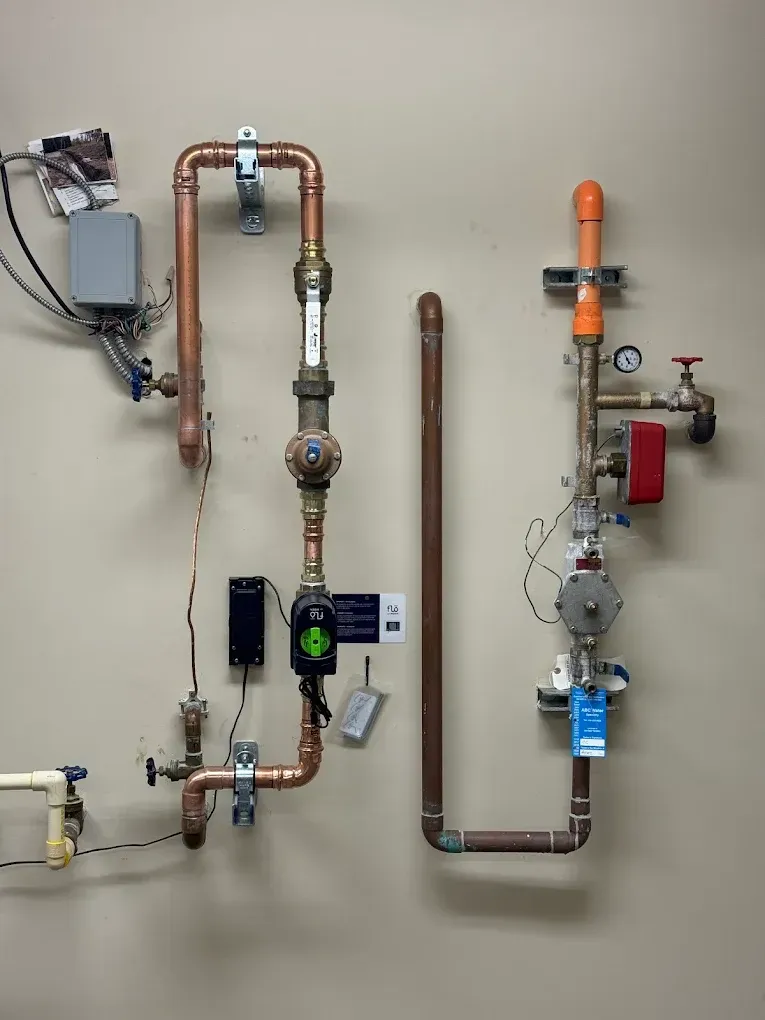 Wall-mounted plumbing and gas piping with valves, meters, and gauges on a utility room wall