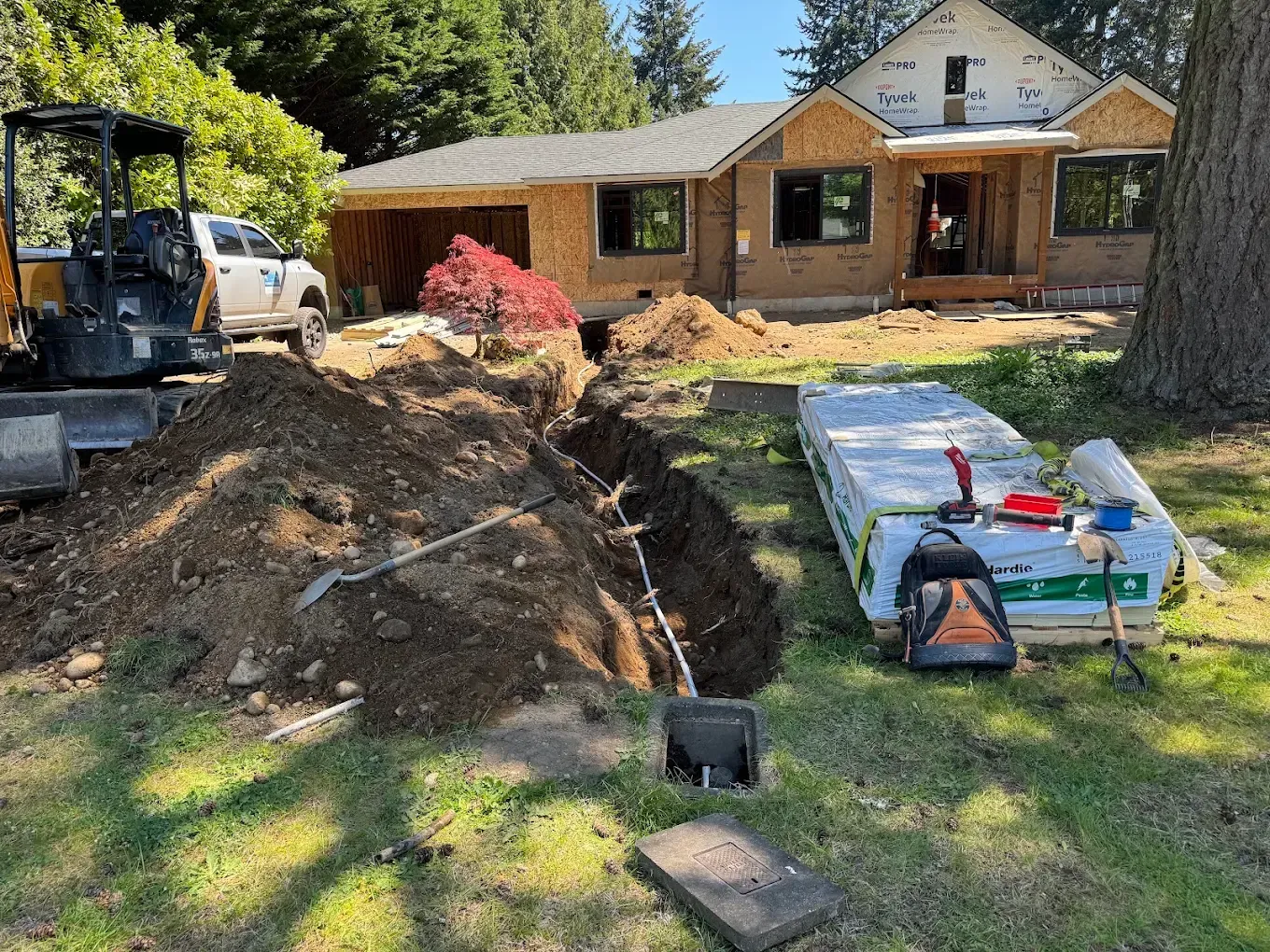 Residential construction site with a large dirt pile, tools on the lawn, and a house under renovation in the background