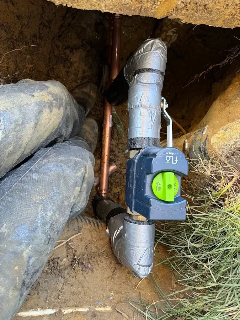 Green outlet mounted on a silver pipe in a rocky outdoor trench
