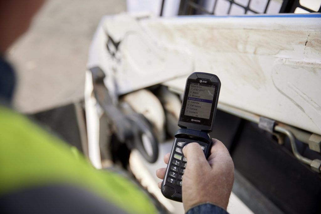 A man is holding a flip phone in front of a vehicle