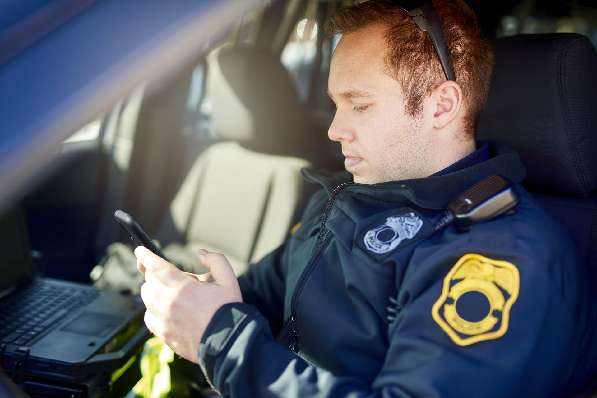 A police officer is wearing a vest with a cell phone attached to it and the words