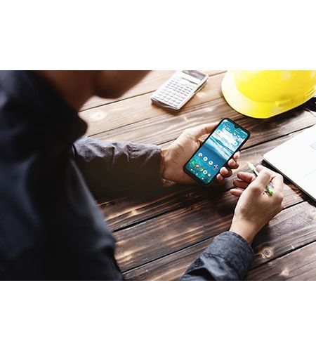 A man is sitting at a wooden table using a cell phone.
