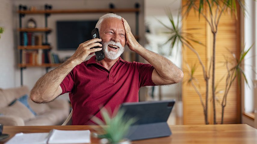 An elderly man is sitting at a table talking on a cell phone.