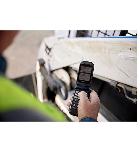 A man is holding a cell phone in his hand in front of a vehicle.