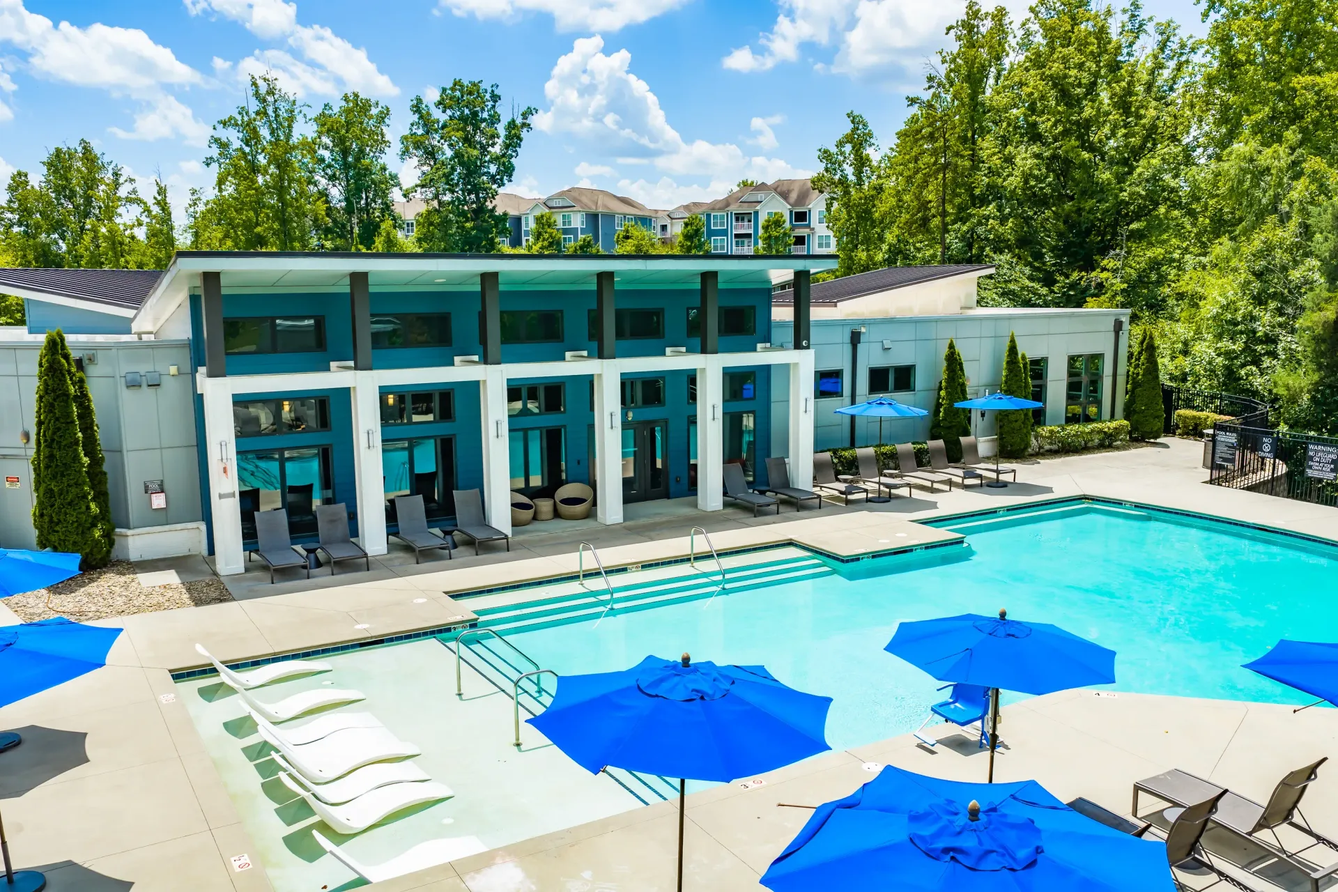 Resort-style swimming pool with lounge chairs and umbrellas next to a modern building.