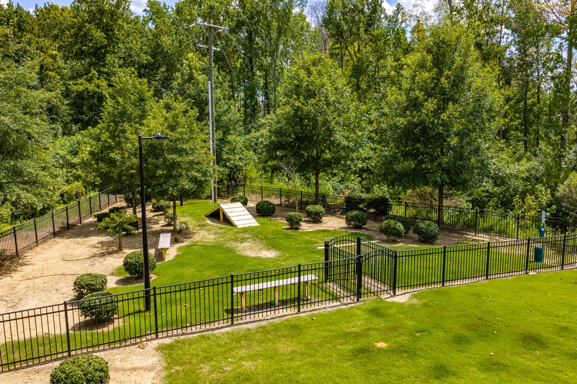 A fenced-in dog park with agility equipment, benches, and grassy areas.