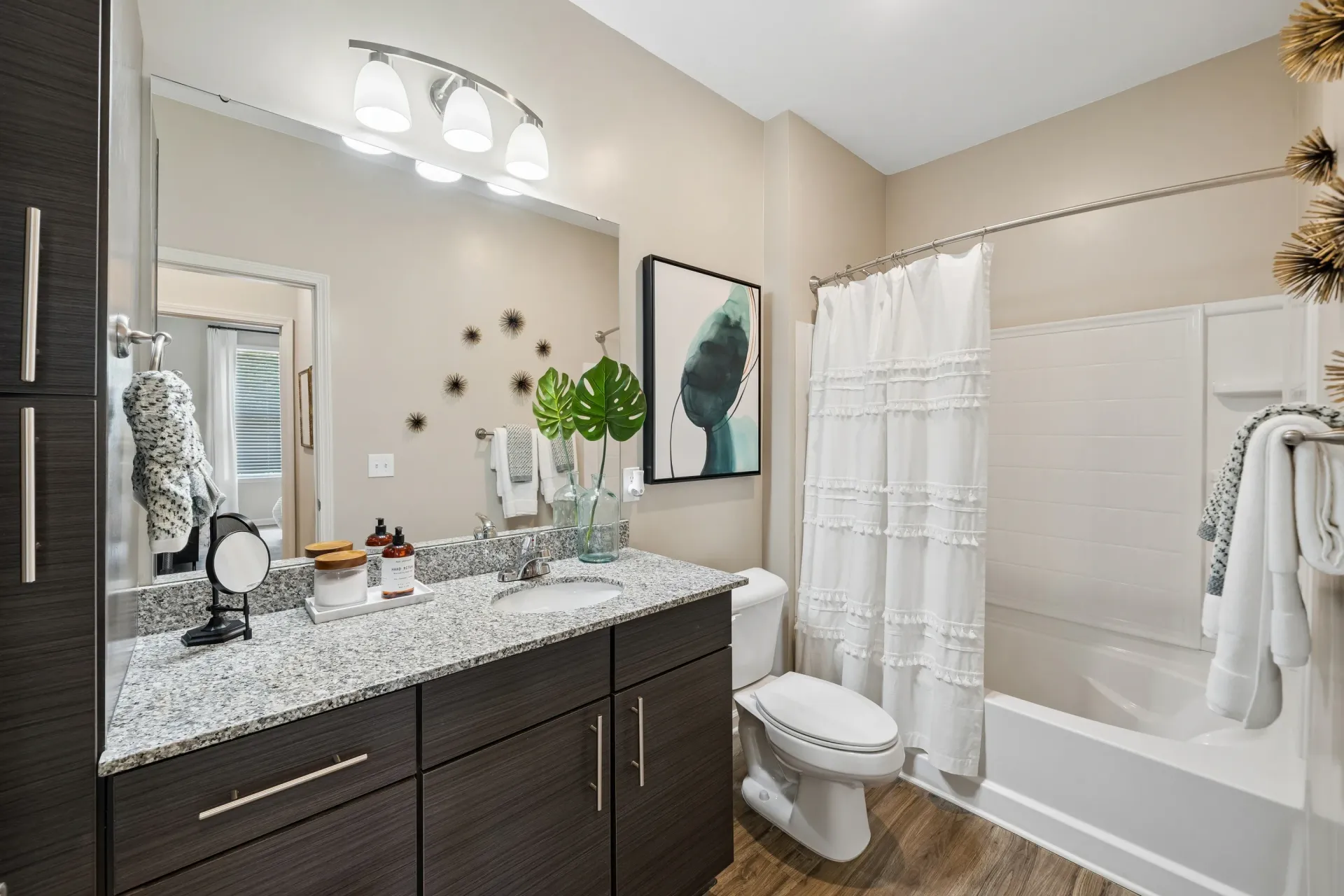 Modern bathroom vanity with granite countertop, vessel sink, and dark wood cabinets. Includes a toilet and a bathtub with a white ruffled shower curtain at Willows at the University in Charlotte, NC.