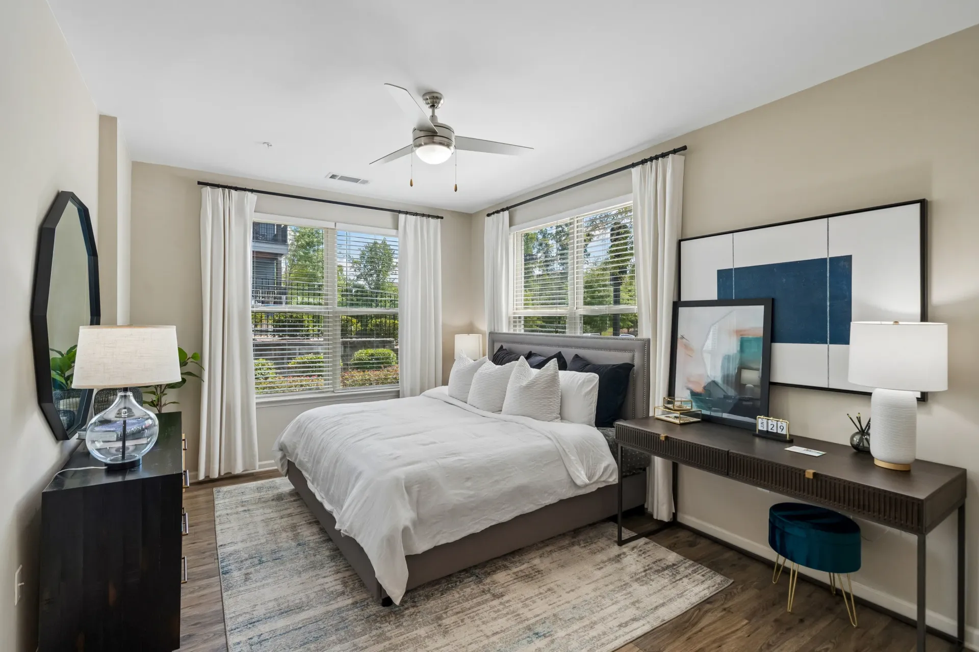 King-size bed with white linens and decorative pillows in a bedroom with a desk and mirror at Willows at the University in Charlotte, NC.