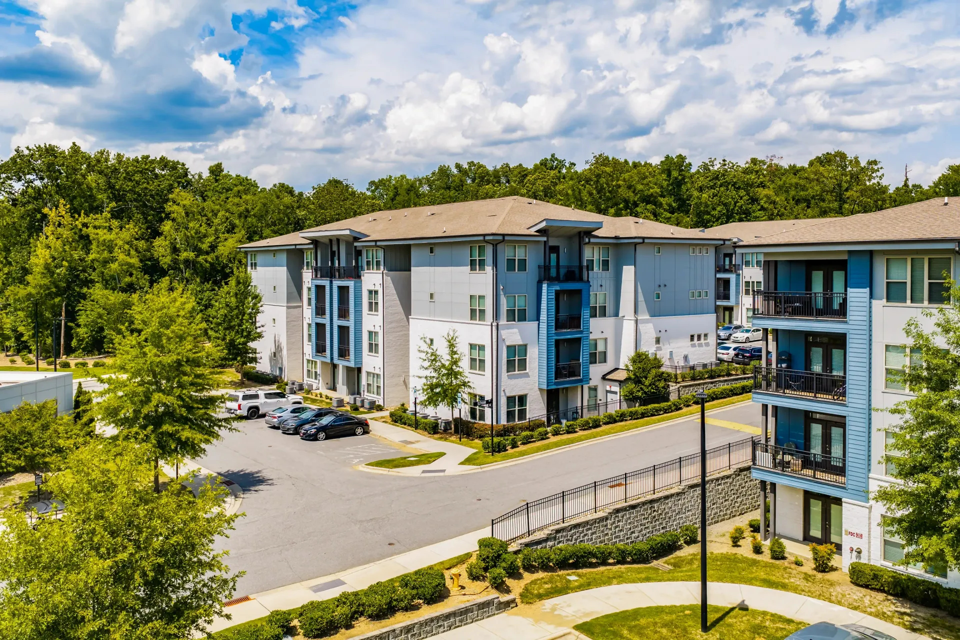 Aerial view of a modern apartment building exterior with blue and grey accents and balconies, surrounded by trees at Willows at the University in Charlotte, NC.