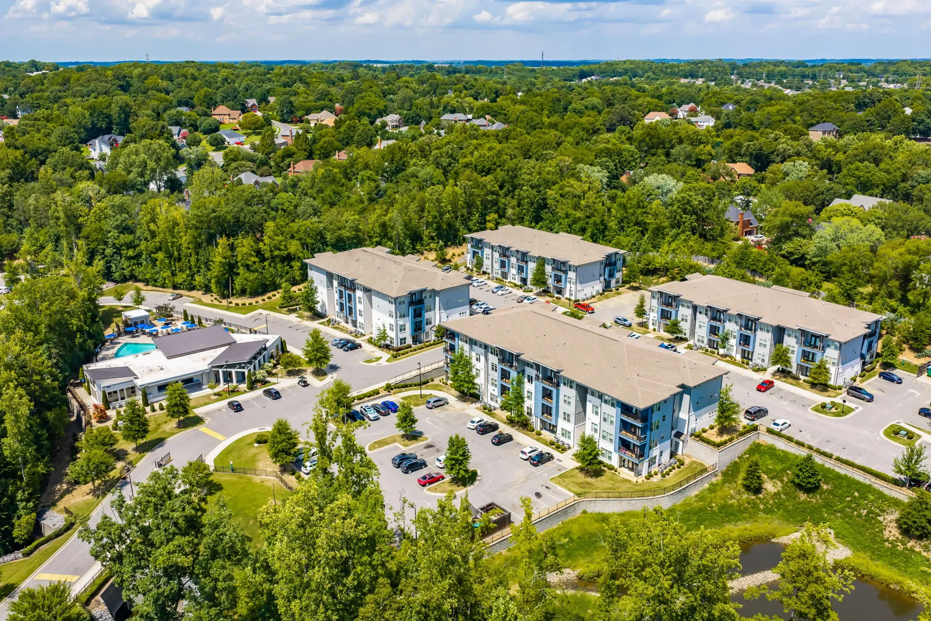 Aerial view of modern apartment buildings with a resort-style pool and lush green surroundings at Willows at the University in Charlotte, NC.