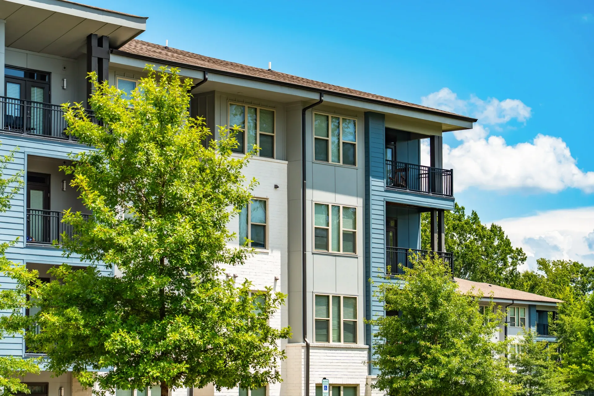 Exterior of apartment building with balconies and trees at Willows at the University in Charlotte, NC.
