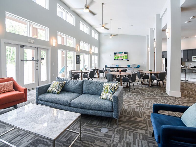 Bright communal lounge with sofas, tables, and a wall-mounted TV at Willows at the University, offering apartments for rent in Charlotte, NC.
