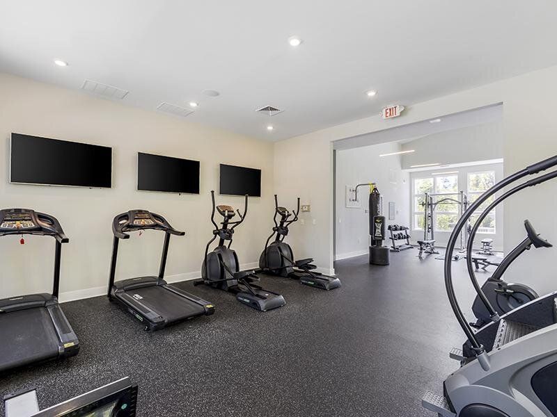 Indoor fitness center with treadmills, ellipticals, and wall-mounted TVs at Willows at the University, offering apartments for rent near UNC Charlotte.