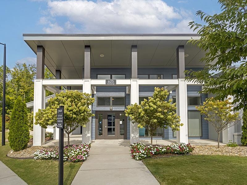 Exterior view of the modern apartment community entrance at Willows at the University, featuring glass doors and a landscaped walkway. Offering one-, two-, and three-bedroom apartments in Charlotte, NC.