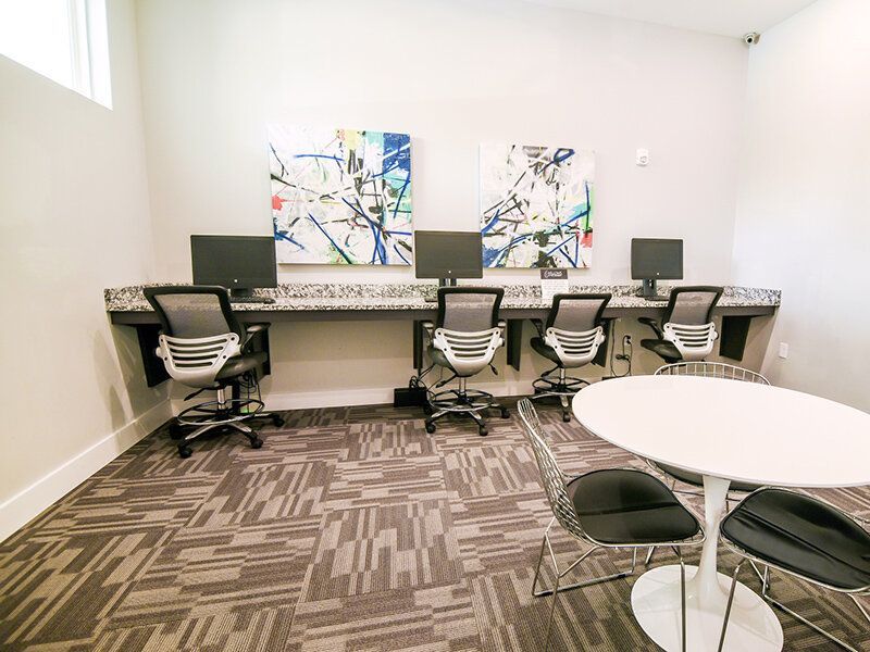 Community computer lab with four workstations along a counter and a round-table seating area at Willows at the University, offering apartments in Charlotte, NC.