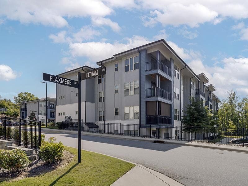 Exterior view of a modern apartment building with a gated entry and street sign poles at Willows at the University, offering apartments near UNC Charlotte.