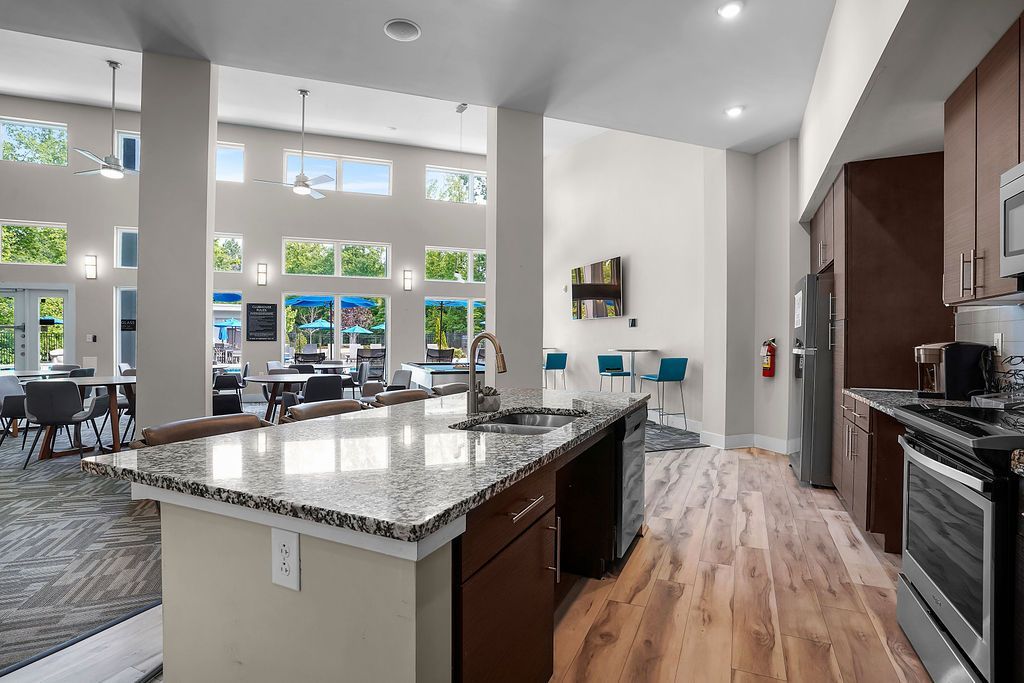 Bright community lounge with a kitchen and large windows at Willows at the University, offering apartments in Charlotte, NC.