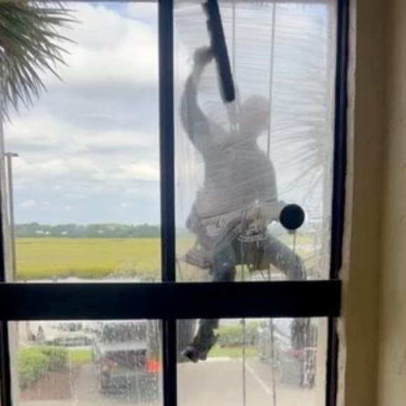 Man cleaning a window with a long tool, outdoors, bright daylight.