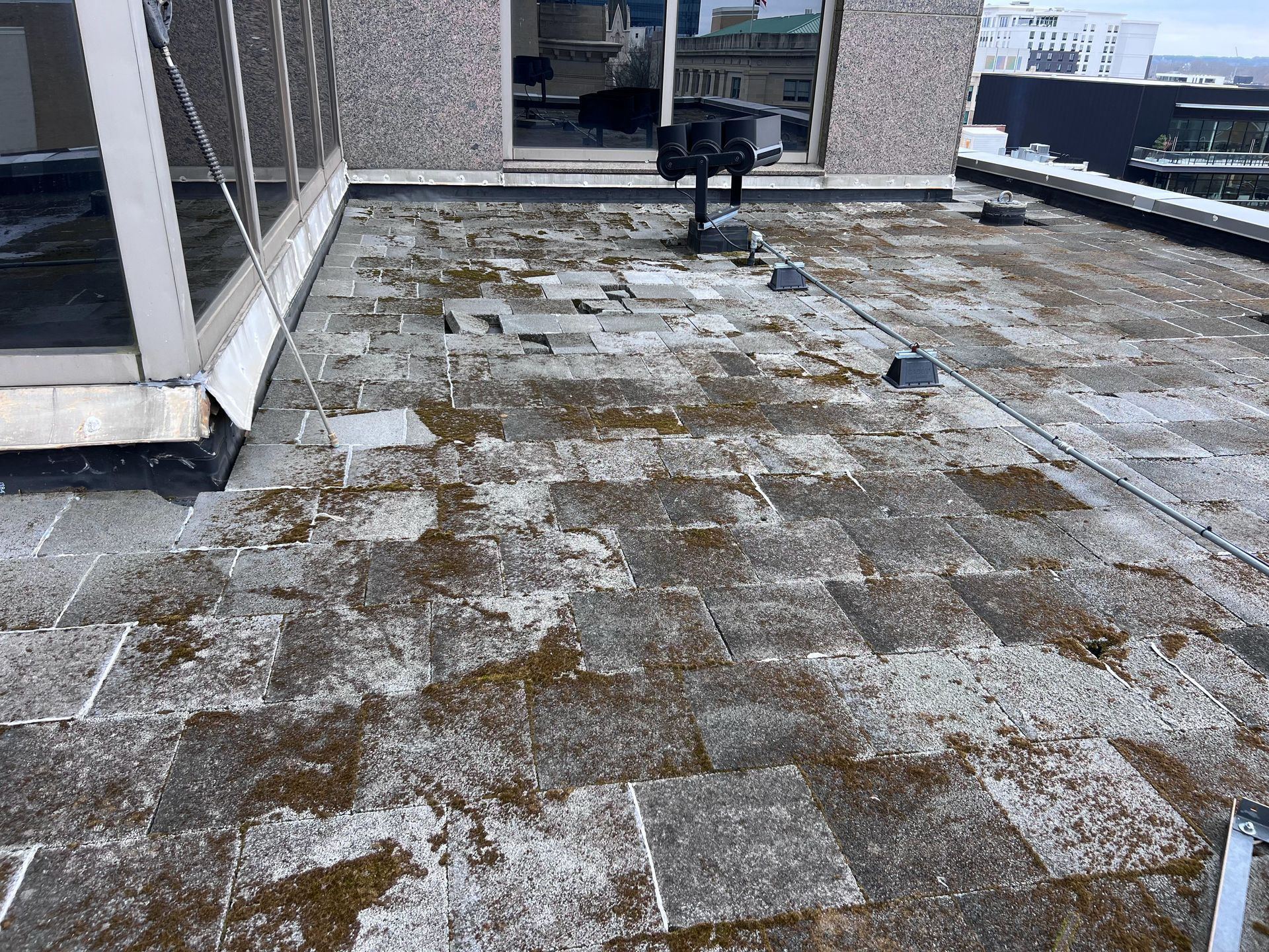 Rooftop with weathered tiles covered in moss, near a window and air conditioning unit.