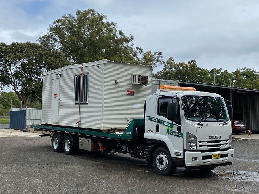 A Bulldozer Is Driving Down A Dirt Road — Taree Tilt Tray Towing In Forster, NSW