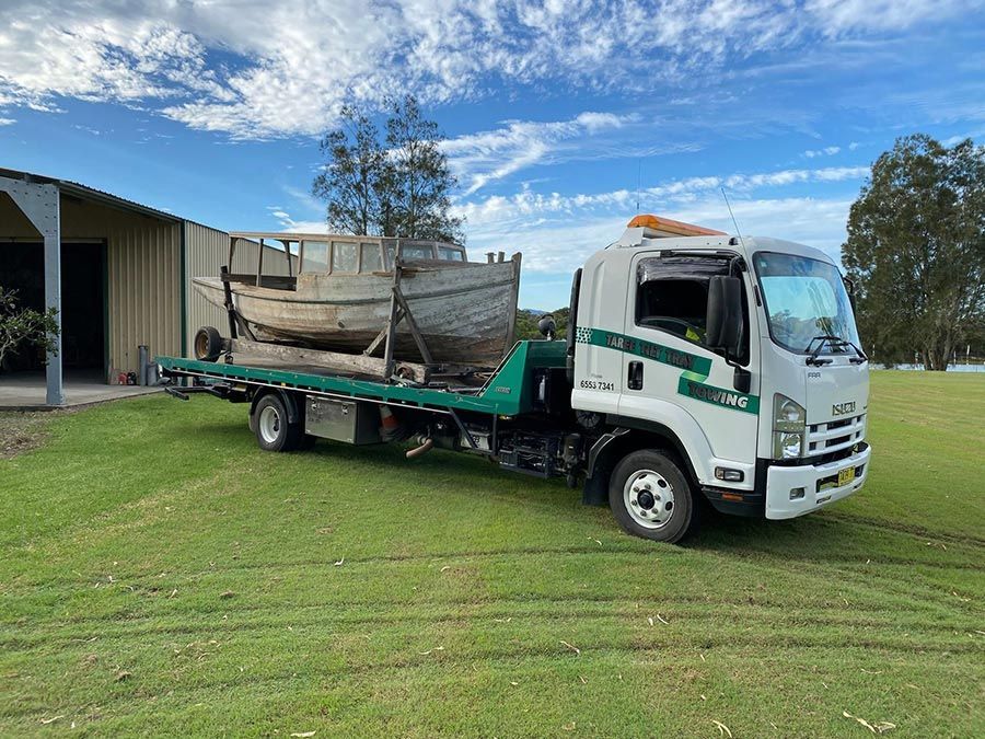 A Tow Truck Is Carrying Three Trucks Down A Road — Taree Tilt Tray Towing In Tuncurry, NSW