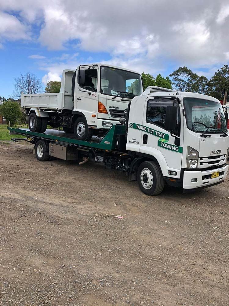 A Tow Truck Is Towing A Camper Down A Street — Taree Tilt Tray Towing In Nabiac, NSW
