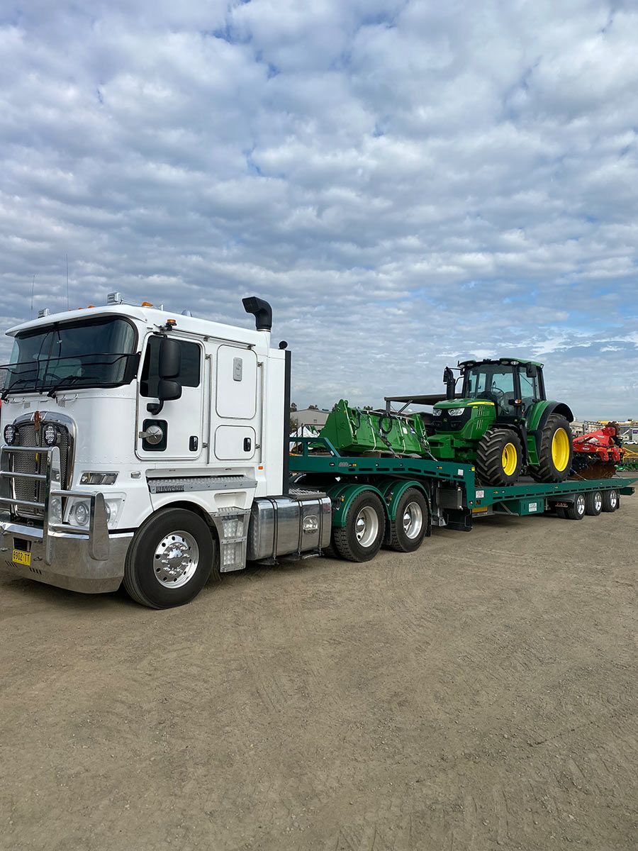 A White Semi Truck Is Carrying A Green Tractor On A Trailer — Taree Tilt Tray Towing In Wingham, NSW