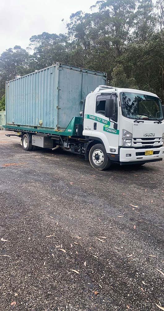 A Tow Truck With A Container On The Back Is Parked In A Gravel Lot — Taree Tilt Tray Towing In Hallidays Point, NSW
