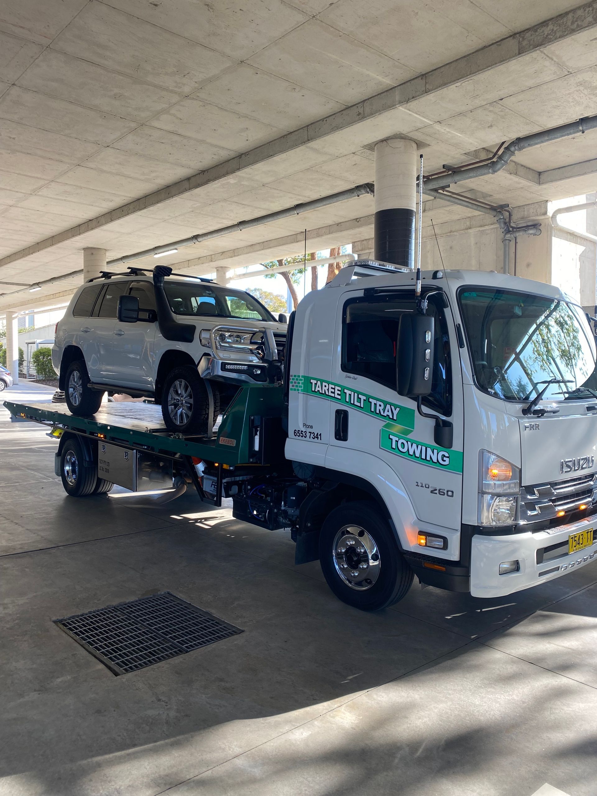 A Tow Truck Is Carrying A Green Excavator On The Back Of It — Taree Tilt Tray Towing In Pampoolah, NSW