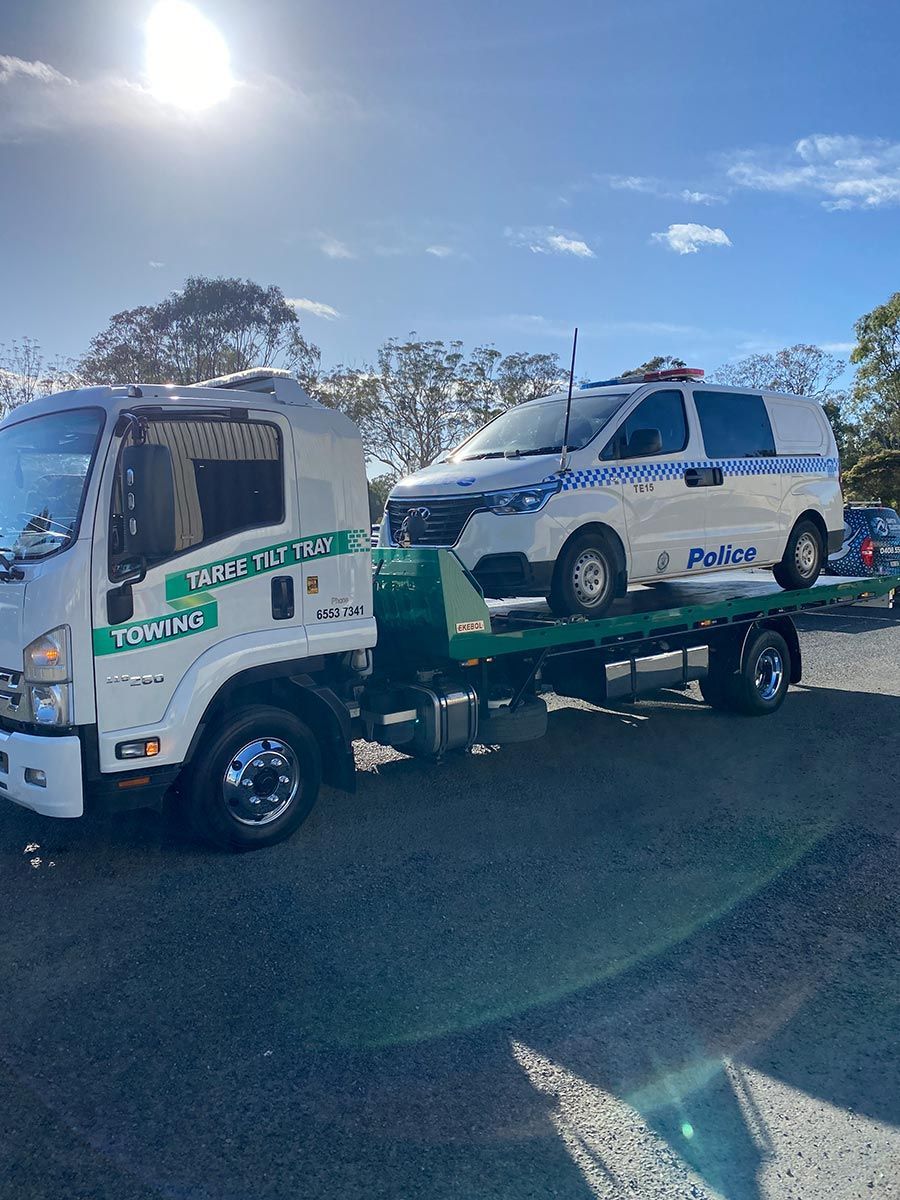 A Tow Truck Is Towing A Police Van In A Parking Lot — Taree Tilt Tray Towing In Coolongoolook, NSW