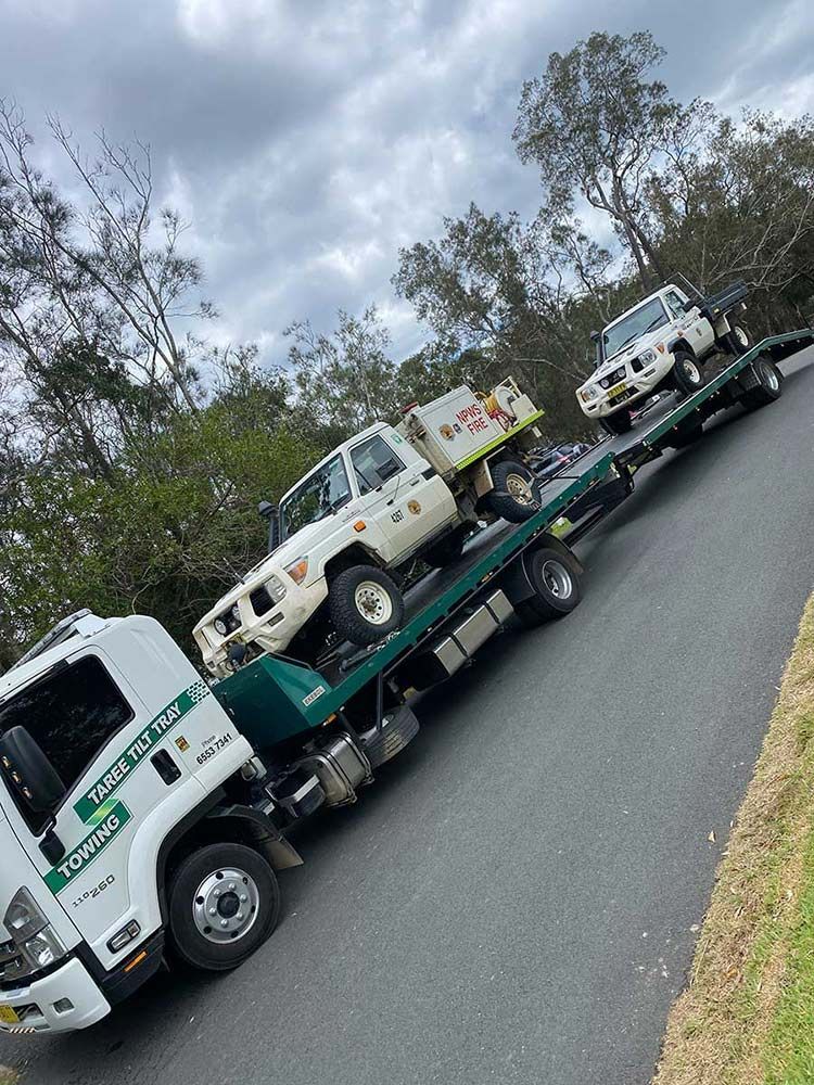 A Tow Truck is Carrying Three Trucks Down a Road — Taree Tilt Tray Towing In Old Bar, NSW
