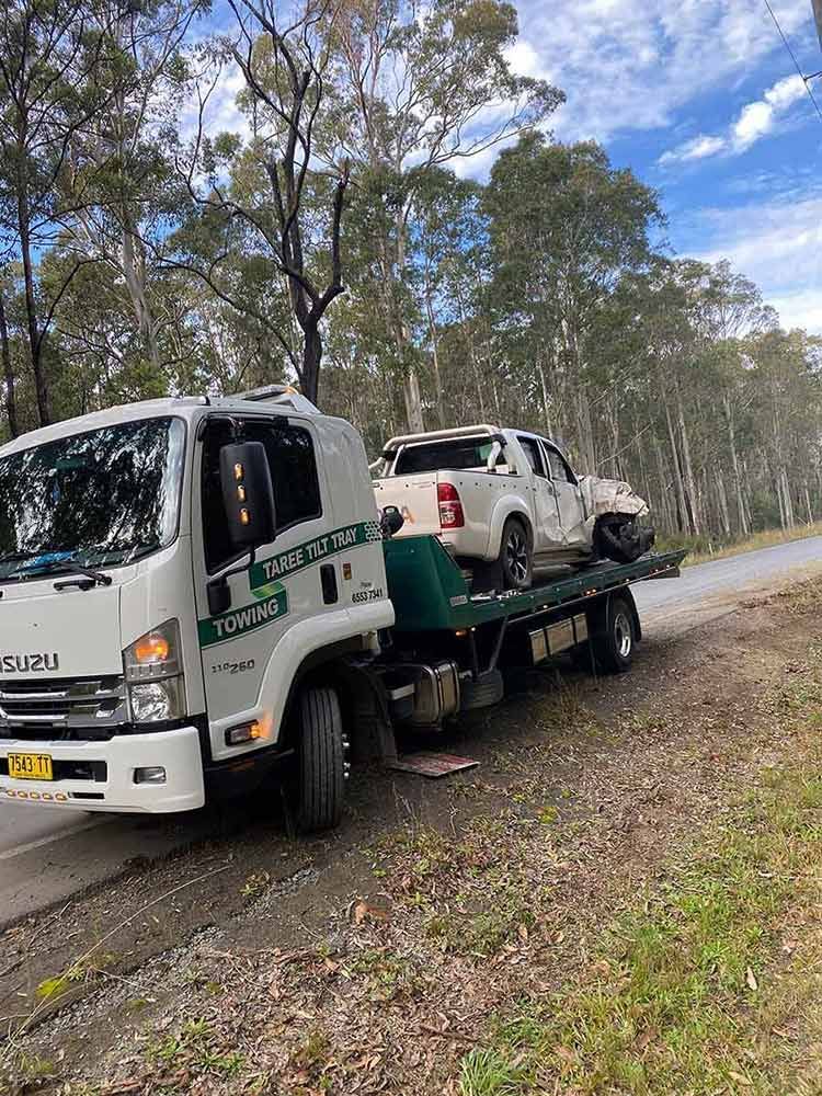 A Tow Truck is Carrying a Broken Car Down a Road — Taree Tilt Tray Towing In Pampoolah, NSW