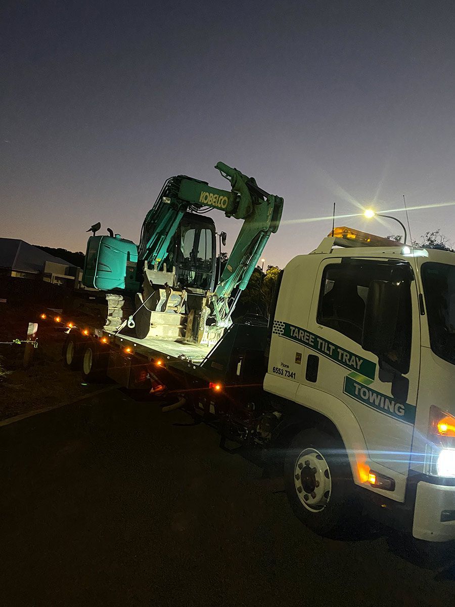 A Tow Truck is Carrying a Green Excavator on the Back of It — Taree Tilt Tray Towing In Taree, NSW