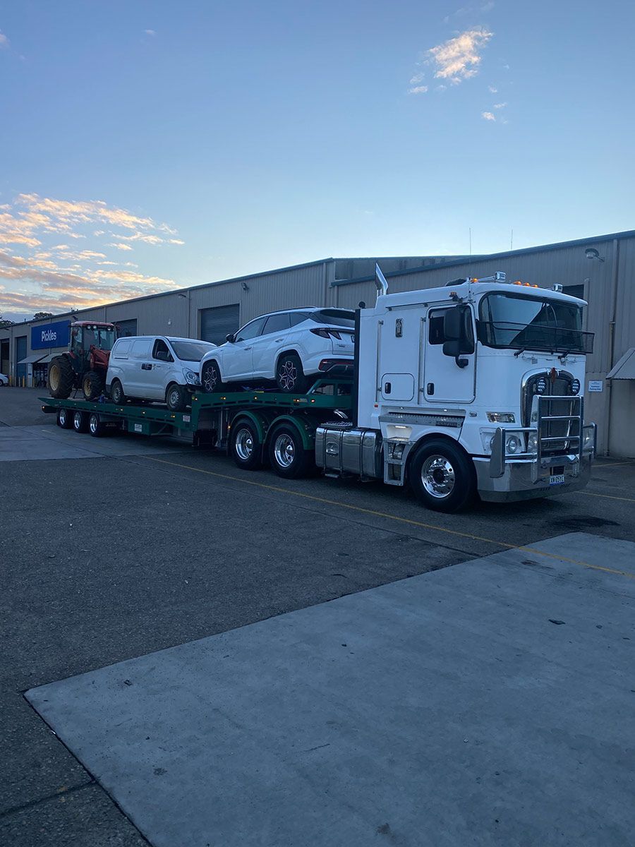 A White Semi Truck Is Carrying Two Cars On A Trailer — Taree Tilt Tray Towing In Wingham, NSW