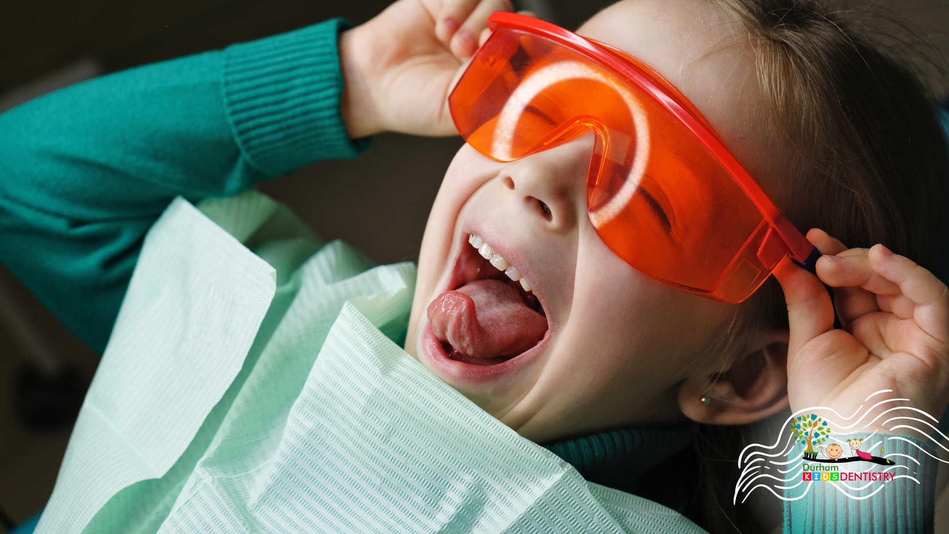 A little girl is sitting in a dental chair wearing safety glasses.