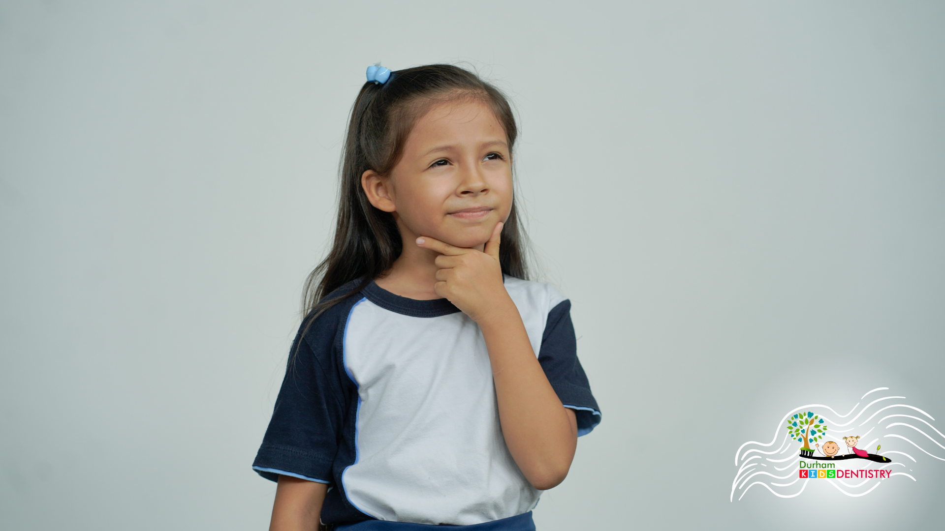 Child in a white and navy shirt posing thoughtfully against a light gray background
