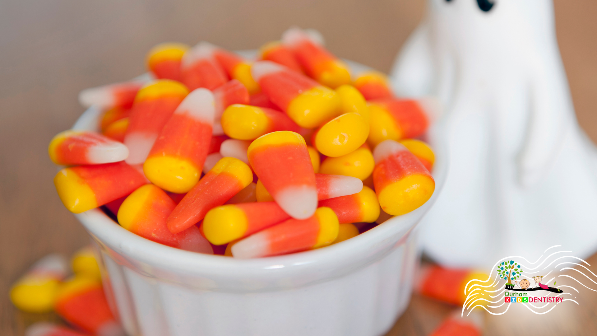 Bowl of orange, yellow, and white candy corn with a blurred white mug in the background