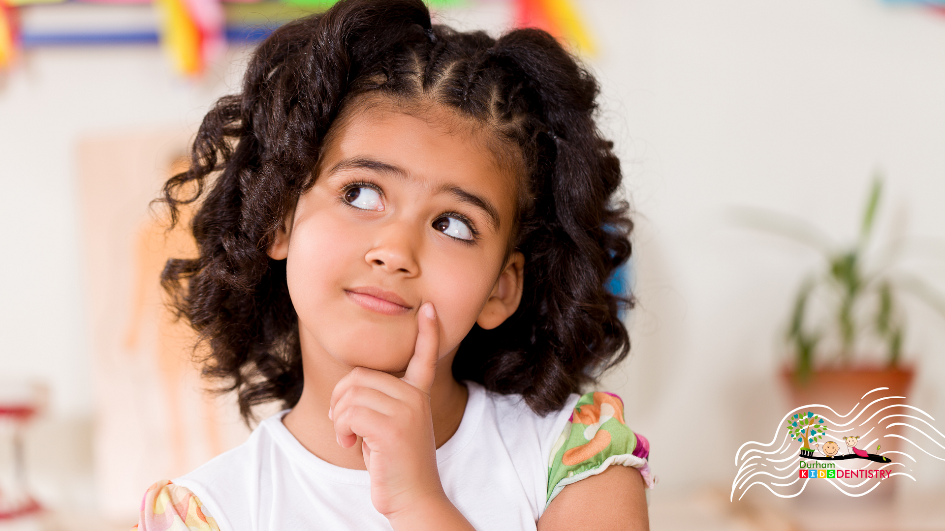 A little girl with curly hair is thinking with her hand on her chin.