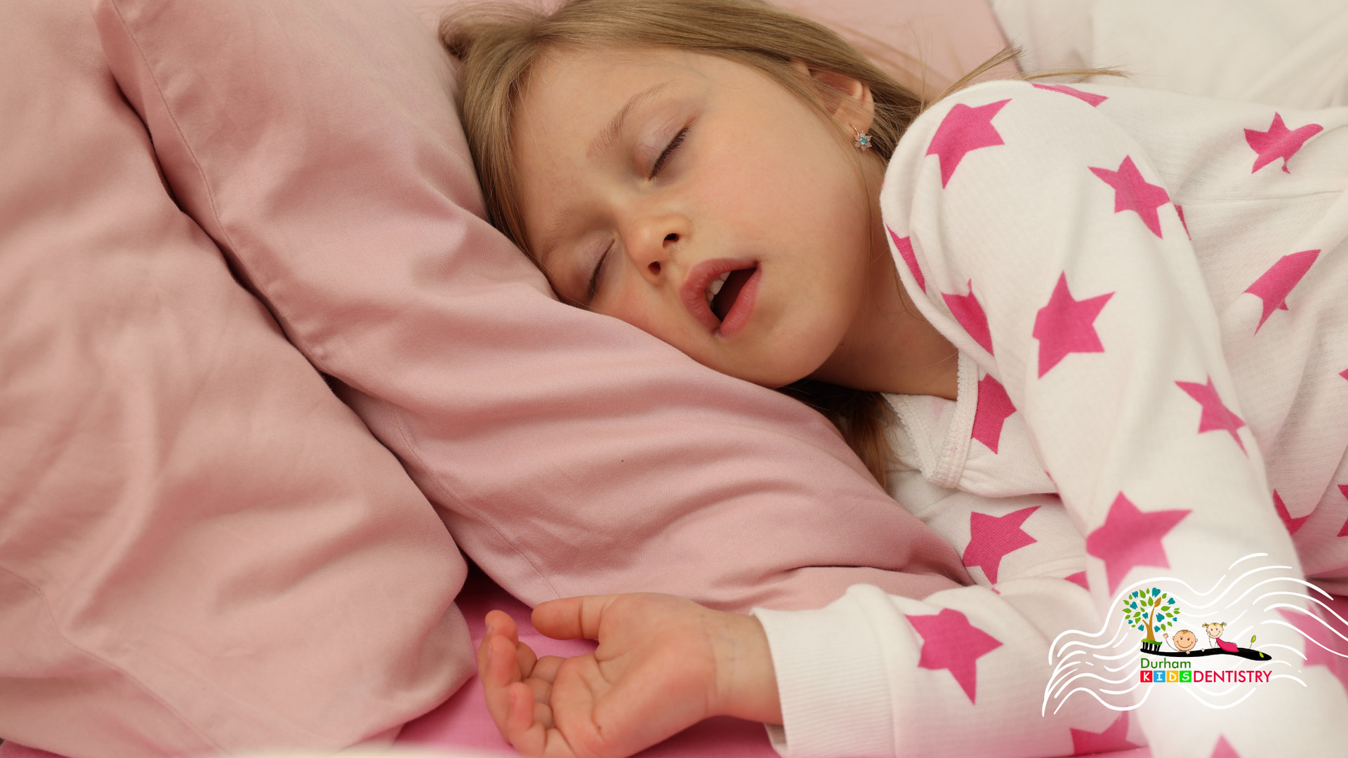 A little girl is sleeping in a bed with a pink pillow.