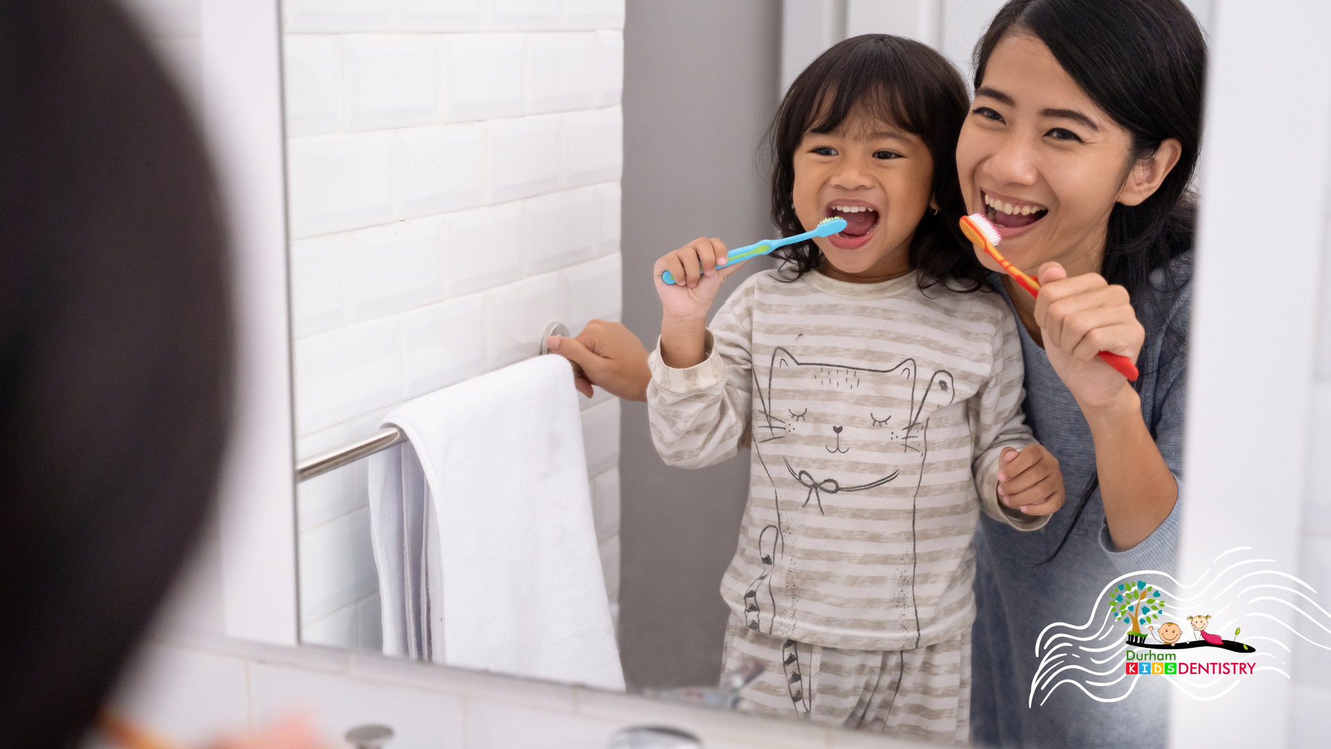 Woman and child brushing teeth together in a bathroom, smiling at the mirror.