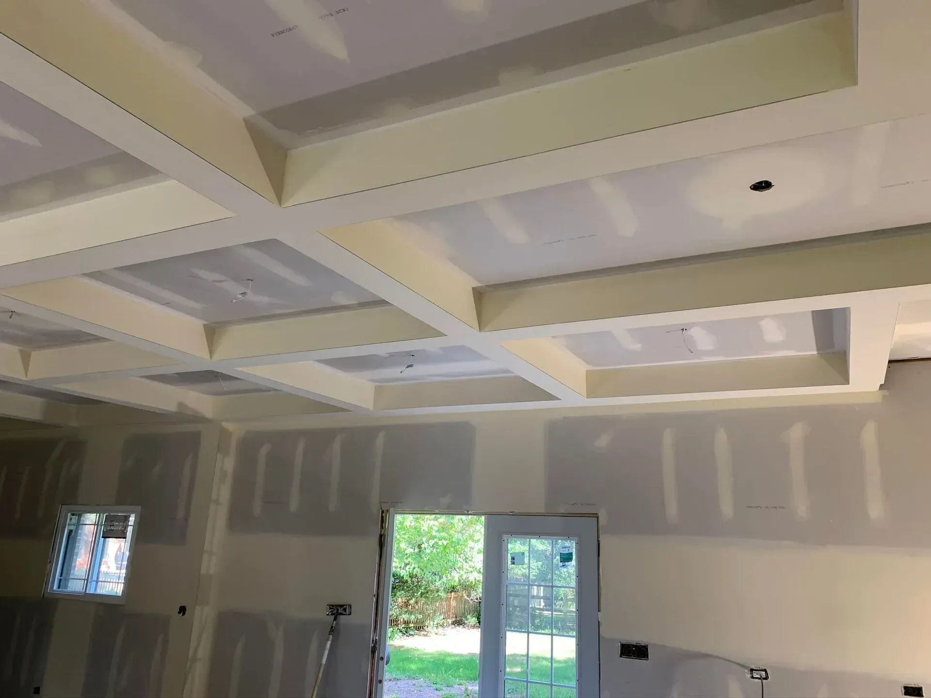 Interior room under construction with white ceiling beams, unfinished walls, and a doorway to outside.