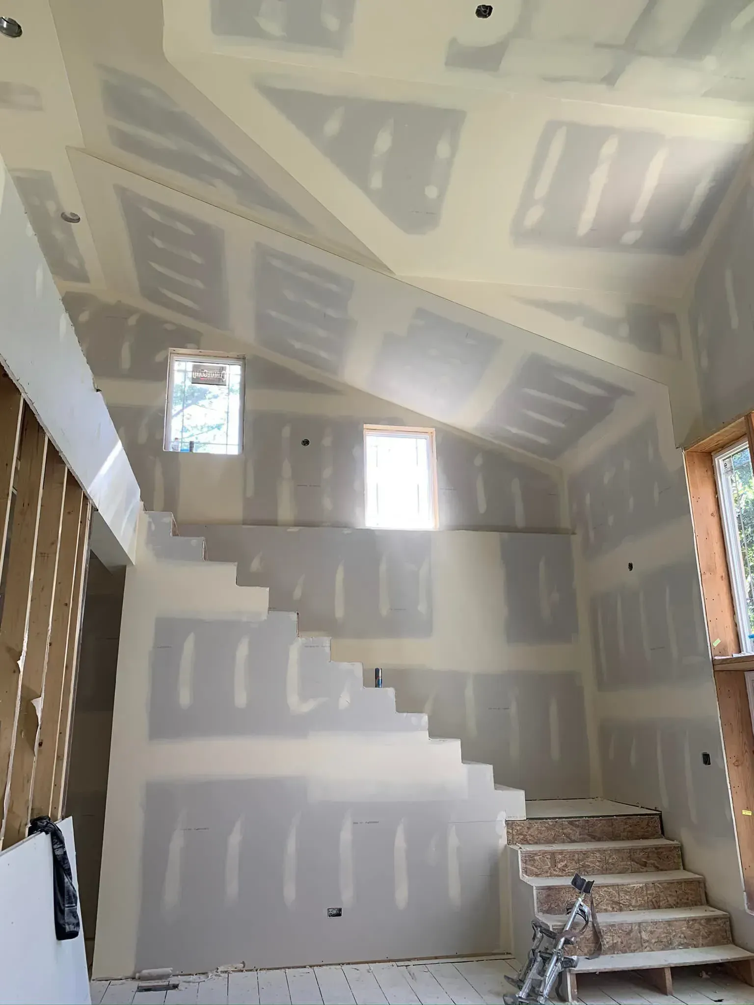 Interior stairwell under construction with unfinished drywall, taped patches, and a small window.