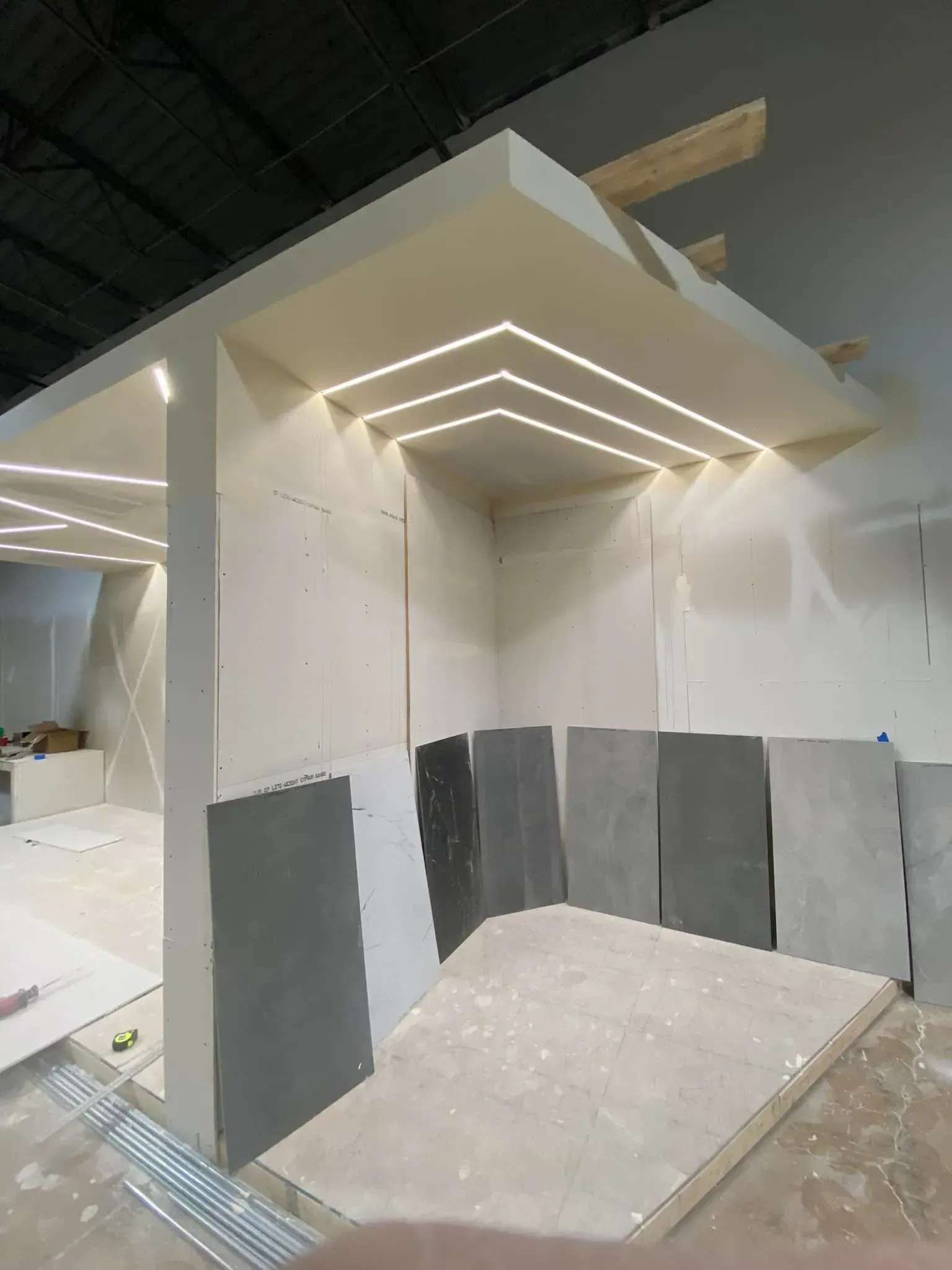 Indoor construction booth with white walls, gray panels, and LED strip lighting at the ceiling.